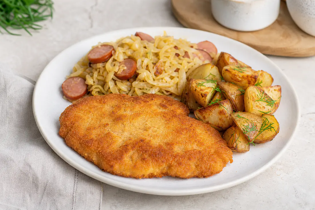 Prato de cozinha polaca simples com panado dourado, batatas rústicas, repolho salteado e rodelas de salsicha