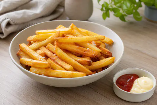 Batatas fritas pré-fritas douradas e estaladiças, acabadas de sair do cesto, numa tigela com sal e um pouco de ketchup ao lado