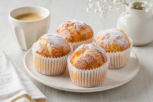 Bolinhos de arroz de pastelaria em forminhas de papel, com o topo alto, dourado e rachado, numa travessa com açúcar em pó