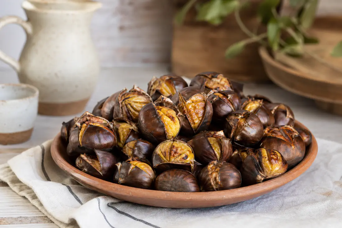 Castanhas assadas inteiras com a casca aberta no golpe, servidas numa travessa de barro com um pano de cozinha