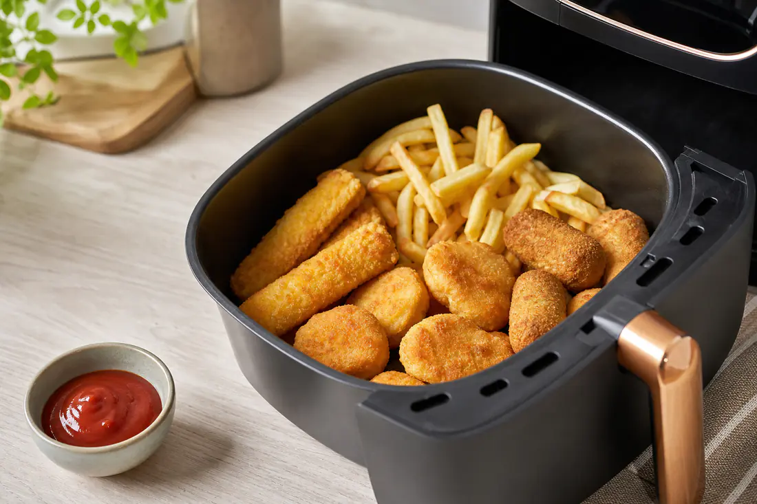 Cesto de airfryer com batatas fritas, douradinhos, nuggets e rissóis dourados acabados de sair, prontos a servir