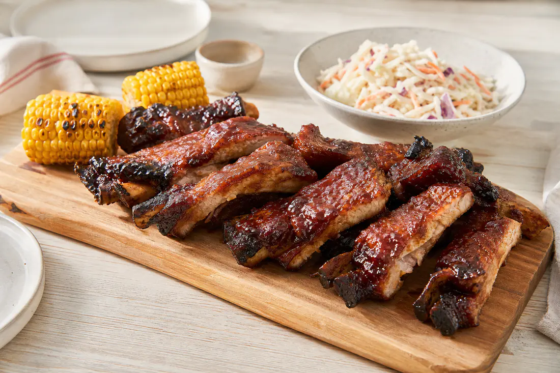 Tiras de entrecosto de porco com osso, caramelizadas com molho barbecue, numa tábua com milho e salada de couve