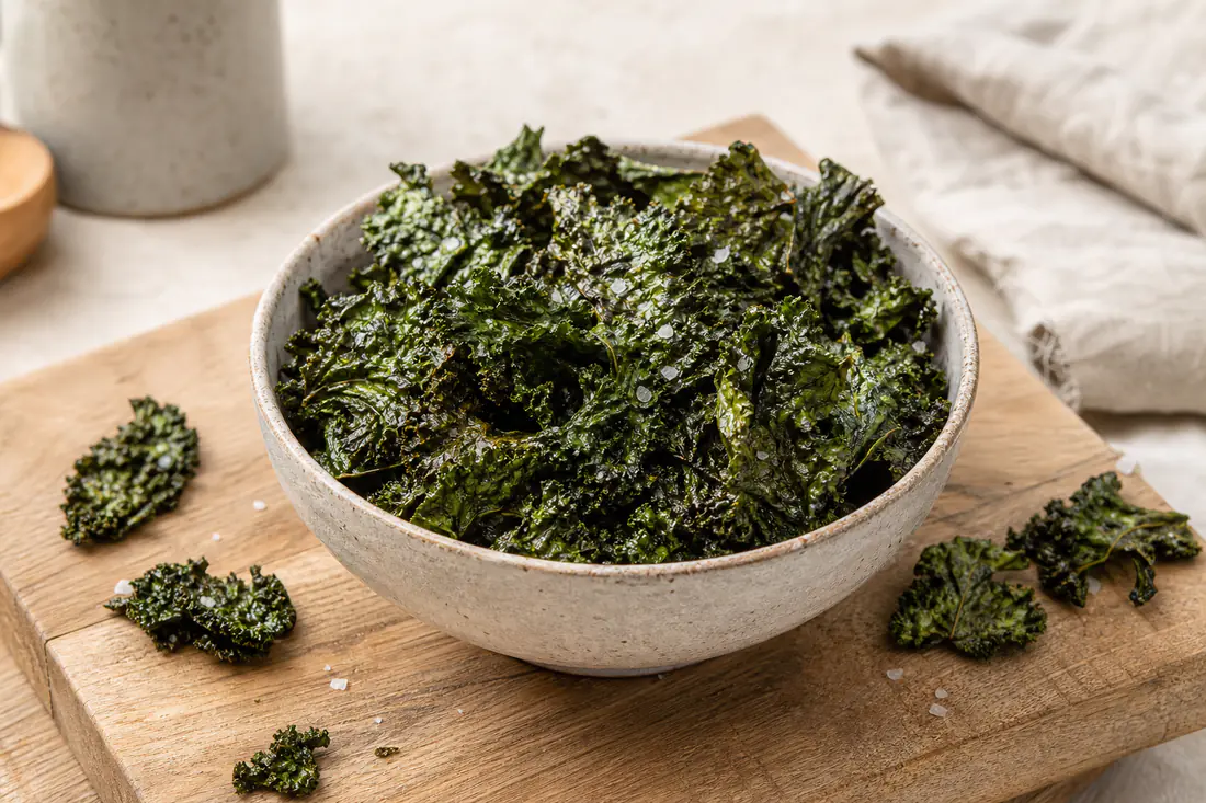 Chips de couve kale verde-escura, finas e crocantes, numa taça de cerâmica com sal em flor
