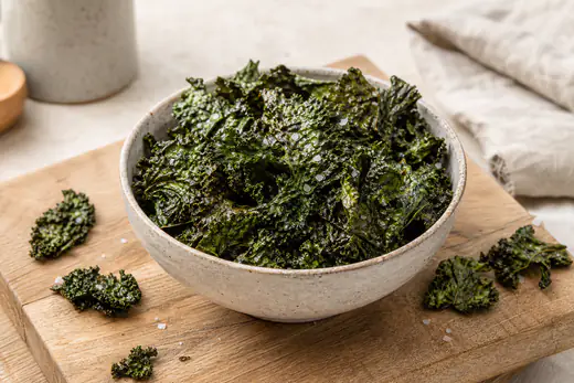 Chips de couve kale verde-escura, finas e crocantes, numa taça de cerâmica com sal em flor