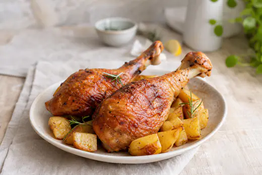 Duas pernas de peru com pele dourada e estaladiça num prato com batatas assadas e ramos de alecrim