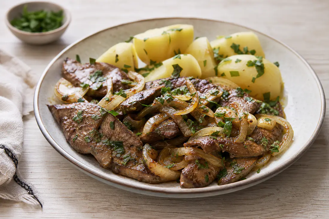 Iscas de fígado de porco douradas, com cebola alourada, servidas num prato com batatas cozidas e salsa