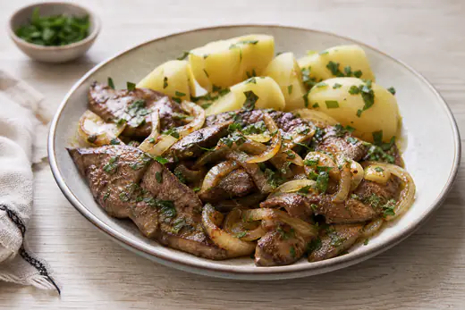 Iscas de fígado de porco douradas, com cebola alourada, servidas num prato com batatas cozidas e salsa