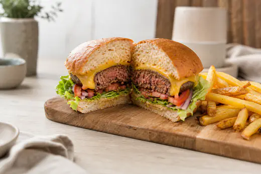 Hambúrguer de vaca com queijo derretido, alface, tomate e cebola num pão tostado, servido com batatas fritas