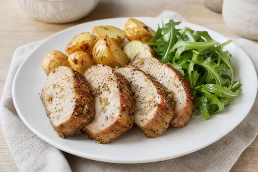 Quatro fatias grossas de lombo de porco douradas, com alho e ervas, servidas com batatas assadas e salada de rúcula