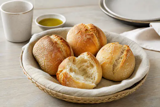 Quatro papo-secos acabados de aquecer, com casca dourada e estaladiça, num cesto de pão forrado com um pano