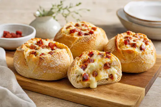 Papo-secos recheados de queijo derretido e pedaços de chouriço, um deles aberto a mostrar o recheio, numa tábua de madeira