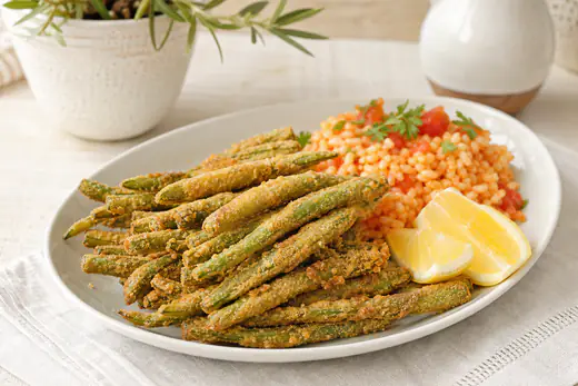 Feijão-verde panado e dourado, os peixinhos da horta, empilhados num prato com rodelas de limão e arroz de tomate