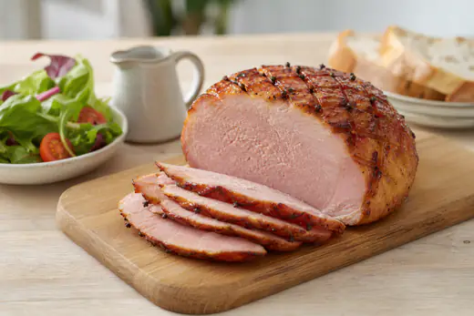 Peça de fiambre glaceada com mel e mostarda, riscada em losangos, parcialmente fatiada numa tábua com salada e pão
