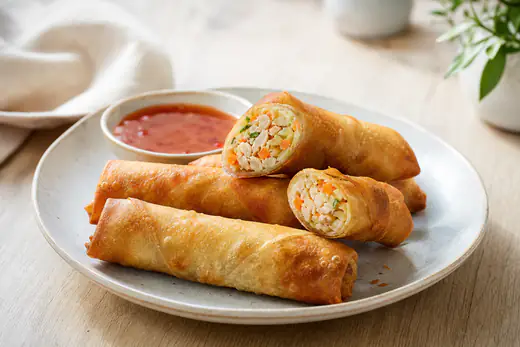 Crepes chineses dourados e estaladiços, um deles cortado ao meio a mostrar o recheio de legumes e frango, com molho agridoce ao lado