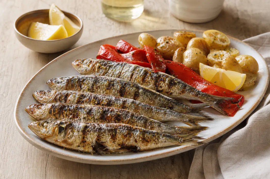 Sardinhas inteiras assadas com a pele dourada e marcas de grelha, servidas com pimentos assados e batatas cozidas