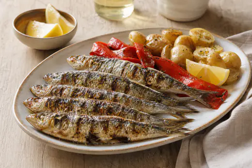 Sardinhas inteiras assadas com a pele dourada e marcas de grelha, servidas com pimentos assados e batatas cozidas