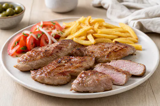 Quatro secretos de porco preto grelhados, cortados em tiras grossas, com batatas fritas, salada de tomate e um raminho de alecrim