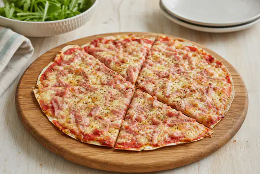 Pizza feita com um wrap fino, com molho de tomate, queijo derretido, tiras de fiambre e orégãos, cortada em fatias numa tábua